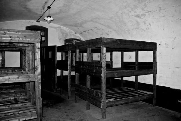 The sleeping quarters with wooden bunks where prisoners stayed. These cramped conditions were a breeding ground for disease and despair, stripping men of their dignity.